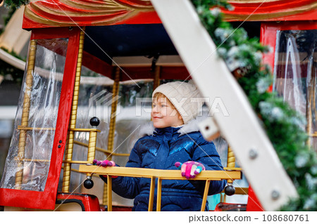 Happy cute preschool girl riding on ferris wheel carousel horse at Christmas funfair or market, outdoors. Little toddler child having fun on traditional family xmas market in Germany Happy cute preschool girl riding on ferris wheel carousel horse at Christmas funfair or market, outdoors. Little toddler child having fun on traditional family xmas market in Germany 108680761
