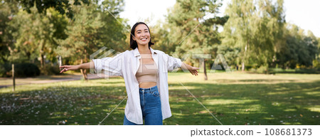Happy asian girl dancing in park, feeling freedom and joy, walking outdoors on sunny day 108681373