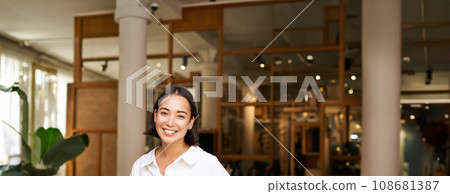 Smiling asian manager, confident woman standing near restaurant entrance, cafe owner welcomes guests Smiling asian manager, confident woman standing near restaurant entrance, cafe owner welcomes guests 108681387