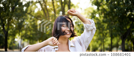 People lifestyle. Portrait of young brunette woman dancing, smiling and laughing, walking in park with hands lift up high, enjoying summer day outside People lifestyle. Portrait of young brunette woman dancing, smiling and laughing, walking in park with hands lift up high, enjoying summer day outside 108681401