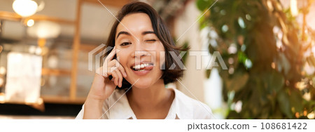 Close up portrait of funny young asian woman, sitting in cafe, chatting lively, smiling at camera Close up portrait of funny young asian woman, sitting in cafe, chatting lively, smiling at camera 108681422