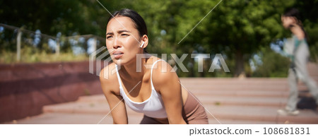 Tired young female runner, asian girl taking break during workout, stop jogging, panting while breathing, running in park 108681831