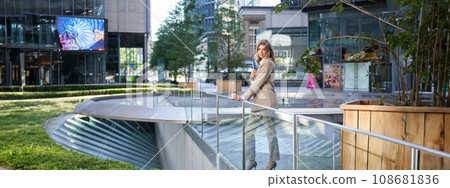 Corporate people. Beautiful business woman with laptop and documents, drinks her coffee in morning near office building, standing in city center 108681836