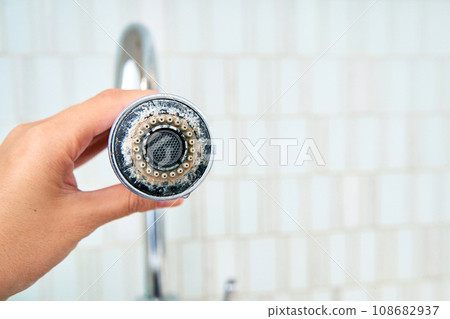A woman is holding a chrome faucet covered with lime scale. 108682937