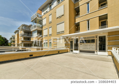 an outside area with some buildings in the background and a white fence on the other side of the building there is a blue sky an outside area with some buildings in the background and a white fence on the other side of the building there is a blue sky 108684403