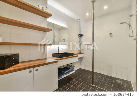 a bathroom with white tiles and wooden shelves on the wall, along with a glass shower stall in the corner a bathroom with white tiles and wooden shelves on the wall, along with a glass shower stall in the corner 108684413