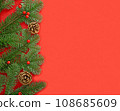 Green fir branches with red berries and brown cones on the left on the red background. 108685609