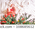 Newborn baby in red clothes located under the decorated christmas tree. 108685612