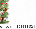 Green branches with red berries and brown cones to the left on white background. 108685624