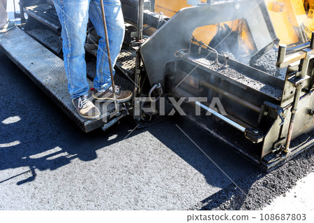 Pavement machine lays fresh asphalt on top of gravel base during construction highway 108687803