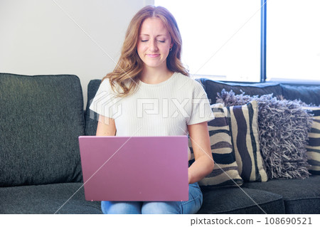 Caucasian woman sitting on a sofa and using a computer (calm) 108690521