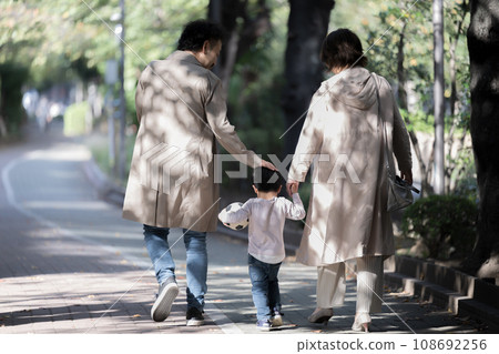 A close family and child walking holding hands, no faces of the family in the back 108692256