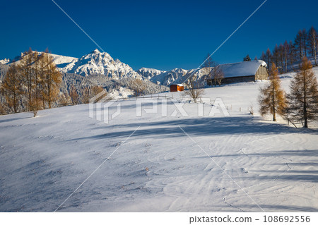 Idyllic winter landscape with snowy wooden hut and high mountains 108692556
