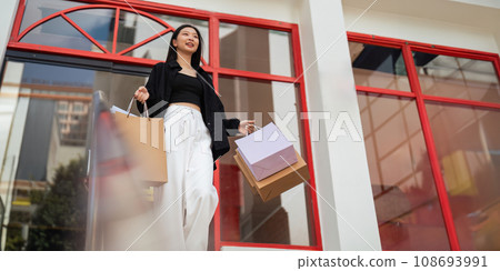 Happy beautiful young stylish woman with shopping bag while walking come out of mall on holiday Black Friday 108693991
