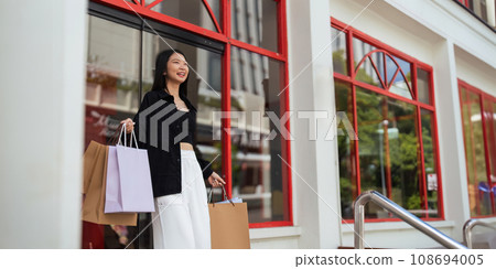 Happy beautiful young stylish woman with shopping bag while walking come out of mall on holiday Black Friday 108694005