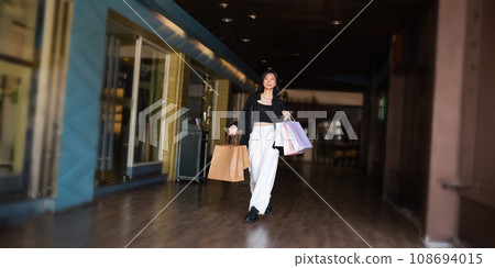 Happy beautiful young stylish woman asian with shopping bag while walking in the mall on holiday Black Friday Happy beautiful young stylish woman asian with shopping bag while walking in the mall on holiday Black Friday 108694015