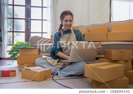 Young woman working online ecommerce shopping at her shop. Young woman seller prepare parcel box of product for deliver to customer. Online selling, ecommerce. Selling products online Young woman working online ecommerce shopping at her shop. Young woman seller prepare parcel box of product for deliver to customer. Online selling, ecommerce. Selling products online 108694141
