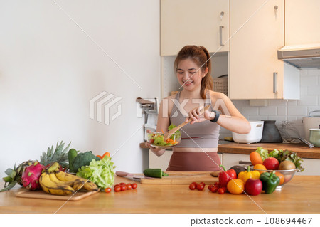 Young woman standing in the kitchen making a salad for health 108694467
