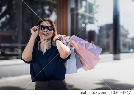 Happy beautiful young stylish woman asian with shopping bag while walking near mall on holiday Black Friday Happy beautiful young stylish woman asian with shopping bag while walking near mall on holiday Black Friday 108694747