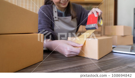 Woman use scotch tape to attach parcel boxes to prepare goods for the process of packaging, shipping, online sale internet marketing ecommerce concept startup business idea Woman use scotch tape to attach parcel boxes to prepare goods for the process of packaging, shipping, online sale internet marketing ecommerce concept startup business idea 108694842