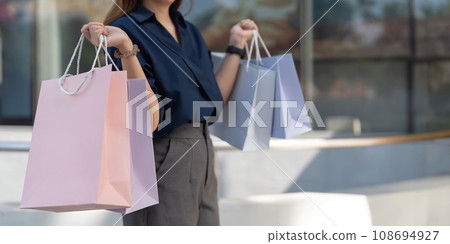 Happy beautiful young stylish woman with shopping bag while walking near mall on holiday Black Friday Happy beautiful young stylish woman with shopping bag while walking near mall on holiday Black Friday 108694927