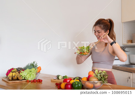 Young woman standing in the kitchen making a salad for health 108695015