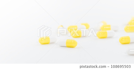 Yellow and white capsules pill spread on white background with shadow and selective focus. Pharmaceutical industry. Yellow and white capsules pill spread on white background with shadow and selective focus. Pharmaceutical industry. 108695503