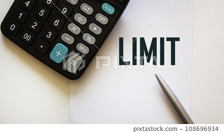 The phrase LIMIT on a white sheet, next to a pen and a calculator 108696934