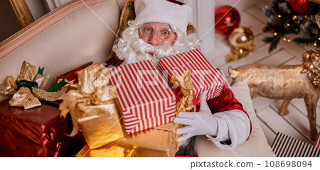 Happy Santa Claus with gifts near fireplace and christmas tree. New year and Merry Christmas concept 108698094
