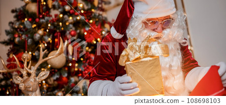 Surprised Santa Claus with glowing gift near christmas tree. New year and Merry Christmas concept Surprised Santa Claus with glowing gift near christmas tree. New year and Merry Christmas concept 108698103