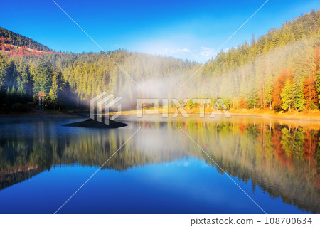 sunny landscape with lake in autumn. fog above the water surface. colorful scenery with sky and trees reflection sunny landscape with lake in autumn. fog above the water surface. colorful scenery with sky and trees reflection 108700634
