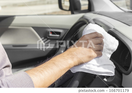 Man's hand wiping down the steering wheel of a light car Man's hand wiping down the steering wheel of a light car 108701179
