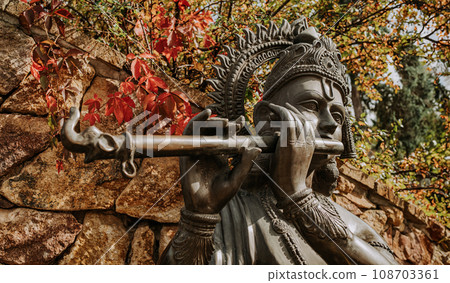 Bronze statue of Lord Krishna playing on flute. Autumn nature. Hinduism religion 108703361