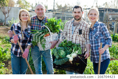 Family of four professional gardeners holding harvest of vegetables and greens 108704423