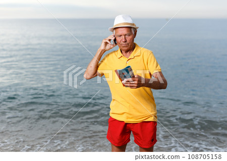 Mature man speaking phone and looking at booklet Mature man speaking phone and looking at booklet 108705158