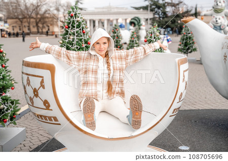 Woman Christmas Square. She sits in a large white cup, dressed in a light suit. With trees decorated with Christmas tinsel in the background Woman Christmas Square. She sits in a large white cup, dressed in a light suit. With trees decorated with Christmas tinsel in the background 108705696