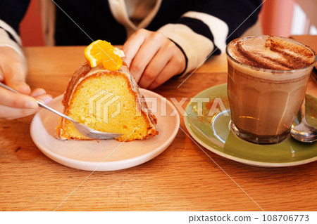 Woman enjoying pumpkin chai latte while eating orange cake at cafe 108706773