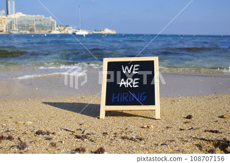 We are Hiring symbol. Concept words We are Hiring on black chalk blackboard blocks. Beautiful sea background. Business and We are Hiring concept. Copy space. 108707156