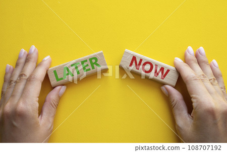 Now vs Later symbol. Concept word Now vs Later on wooden blocks. Businessman hand. Beautiful yellow background. Business and Now vs Later concept. Copy space 108707192