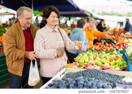 Elderly man and a woman buy apples at an open-air market 108707607