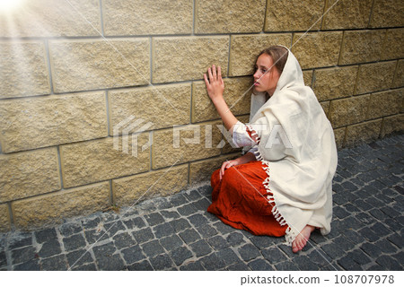 A girl in poor clothes sits on the ground 108707978