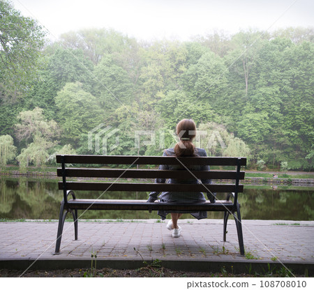Lonely girl on a bench by the lake Lonely girl on a bench by the lake 108708010