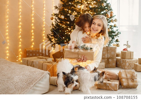 Portrait of a little girl celebrating Christmas with her dogs. Girl and sitting near Christmas tree and posing for a photo. Kid wearing beige knitted clothes. Portrait of a little girl celebrating Christmas with her dogs. Girl and sitting near Christmas tree and posing for a photo. Kid wearing beige knitted clothes. 108708155