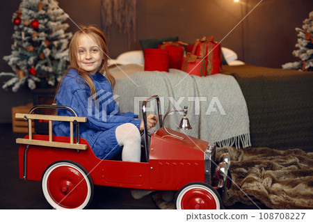 Child in a blue sweater. Daughter sitting near Christmas tree. 108708227