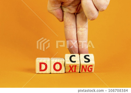 Docs or doxing symbol. Concept words Docs Doxing on wooden block. Beautiful orange table orange background. Businessman hand. Business docs or doxing concept. Copy space. Docs or doxing symbol. Concept words Docs Doxing on wooden block. Beautiful orange table orange background. Businessman hand. Business docs or doxing concept. Copy space. 108708384