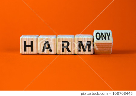From harm to harmony. Turned a wooden cube and changed word harm to harmony. Beautiful orange table, orange background. Business and harm or harmony concept. Copy space. 108708445