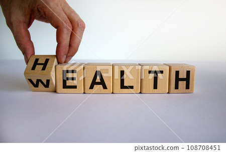 Hand is turning a cubes and changes the word 'health' to 'wealth' or vice versa. Beautiful white background, copy space. Business concept. Hand is turning a cubes and changes the word 'health' to 'wealth' or vice versa. Beautiful white background, copy space. Business concept. 108708451