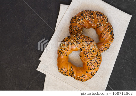 Two tasty sesame bagels. Black background and linen napkin. Type of baking. Top view, copy space. Two tasty sesame bagels. Black background and linen napkin. Type of baking. Top view, copy space. 108711862