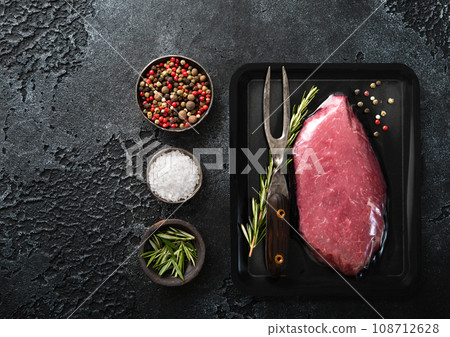 Raw beef steak sirloin fillet sealed in vacuum tray with pepper,rosemary and barbeque fork Raw beef steak sirloin fillet sealed in vacuum tray with pepper,rosemary and barbeque fork 108712628