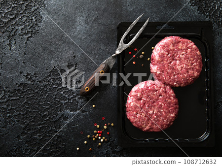 Raw minced beef burgers in plastic vacuum tray on black stone background with fork. Raw minced beef burgers in plastic vacuum tray on black stone background with fork. 108712632